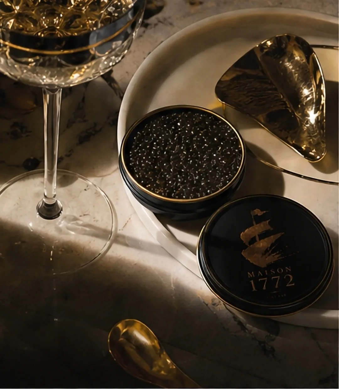 Open caviar tin beside a crystal coupe on marble