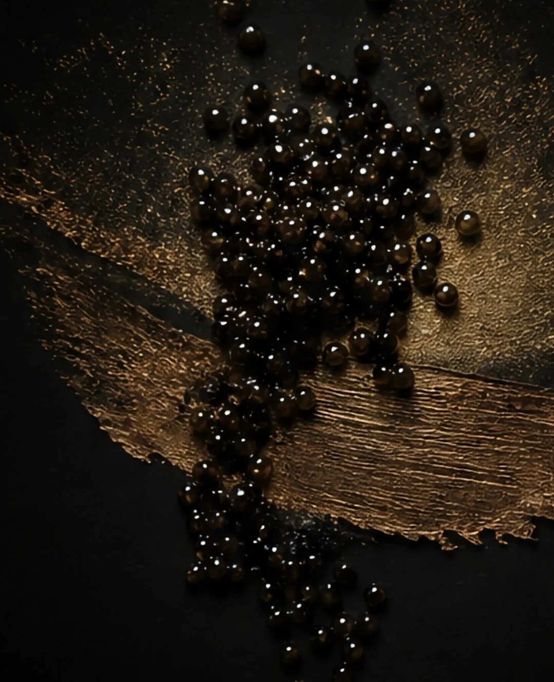 Caviar pearls on dark surface with gold paint stroke