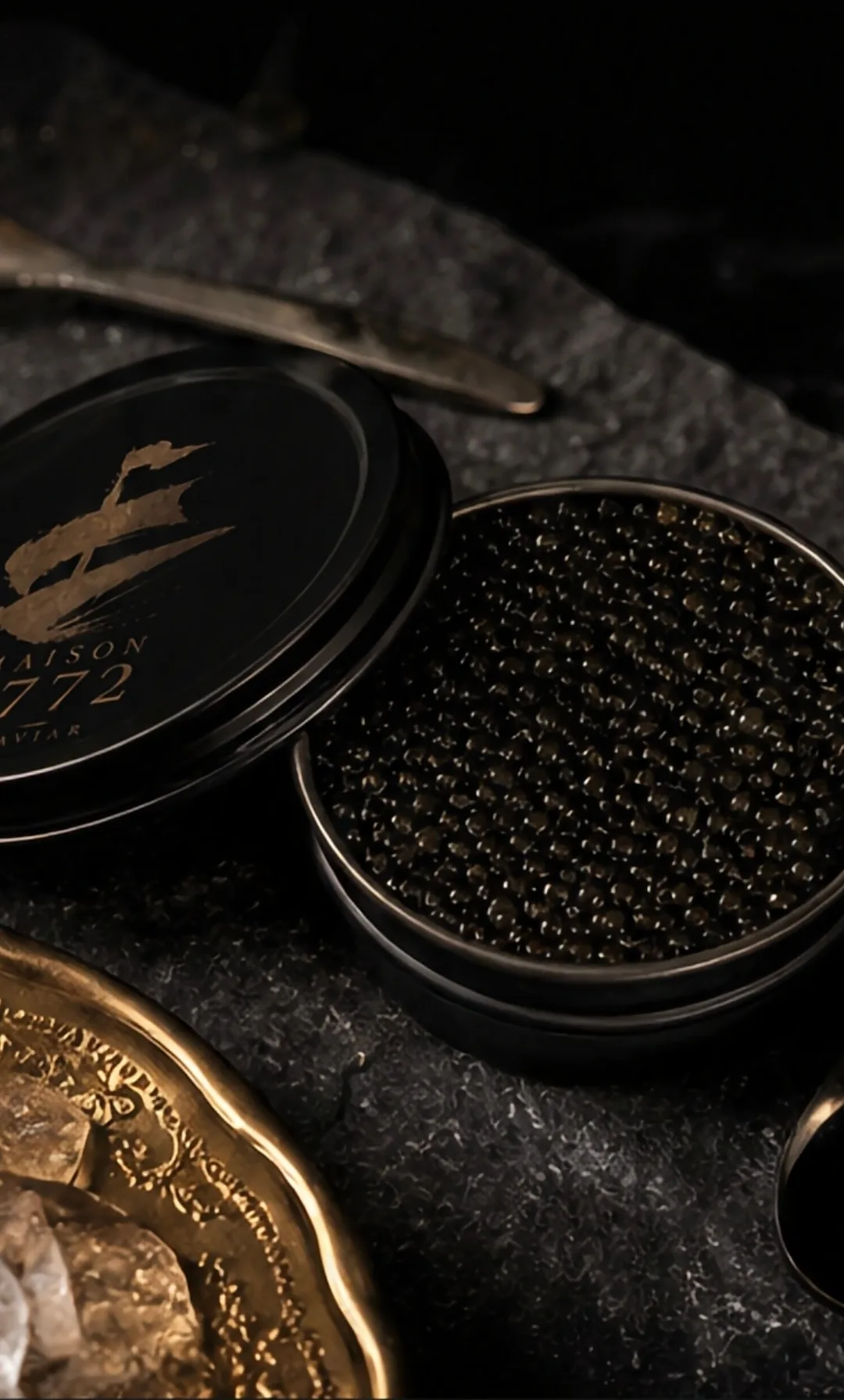 Open caviar tin with gold spoon and ice bowl on stone surface