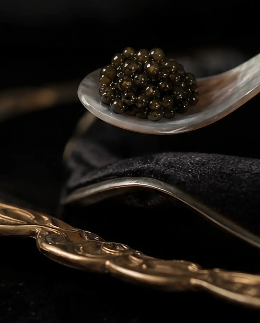 Mother-of-pearl spoon holding caviar beside a gold spoon