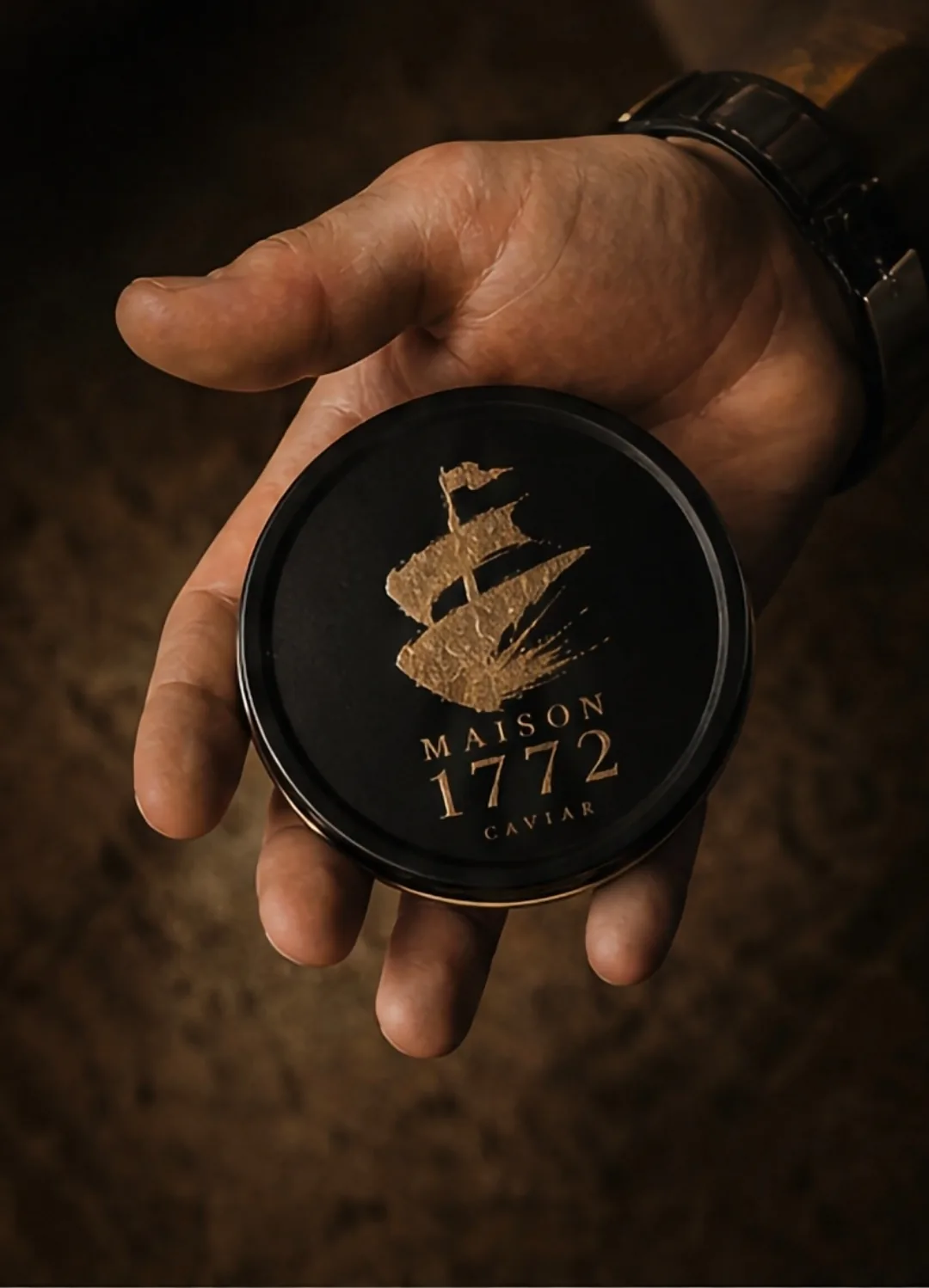 A hand holding a black Maison 1772 caviar tin