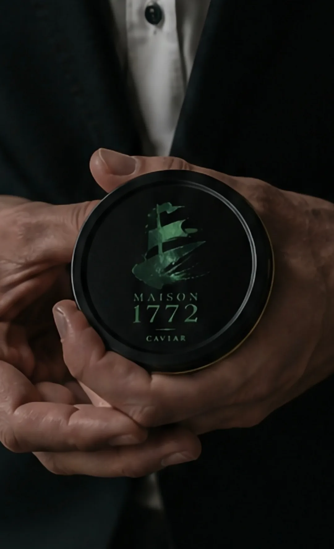 Hands in a dark suit holding a Maison 1772 caviar tin